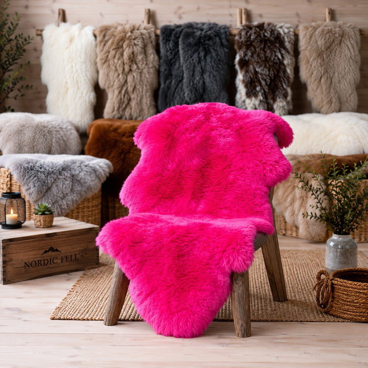 BillyGreen Premium Schaffell in leuchtendem Pink auf einem Holzstuhl in gemütlicher Wohnumgebung mit weiteren Fellen