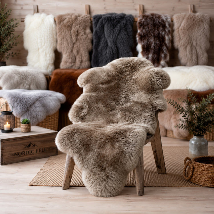 BillyGreen Premium Schaffell in Beige auf einem Holzstuhl vor einer Wand mit verschiedenen Naturfell-Varianten