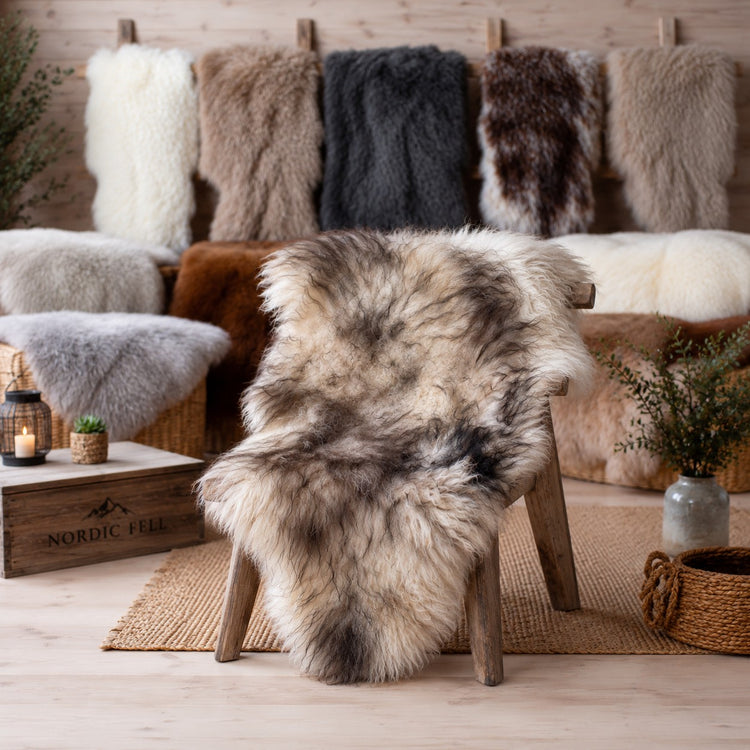 BillyGreen Premium Schaffell in Beige und Braun auf einem Holzstuhl, umgeben von weiteren Naturfellen im Hintergrund.